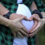mujer embaraza y su pareja formando un corazon encima del vientre de la la madre